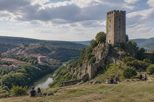 Day visitors on a grass slope below a tall square medieval tower on a rocky hill, Baldwin's Tower