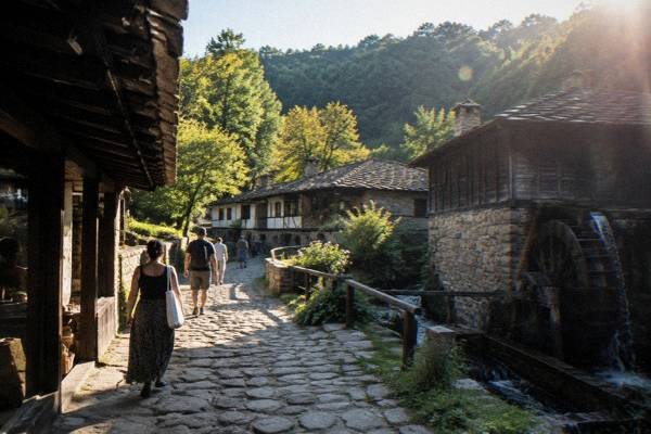 Visitors in a cobbled lane of low stone-and-timber workshops in an open-air village museum, early in the day, Etar Architectural-Ethnographic Complex