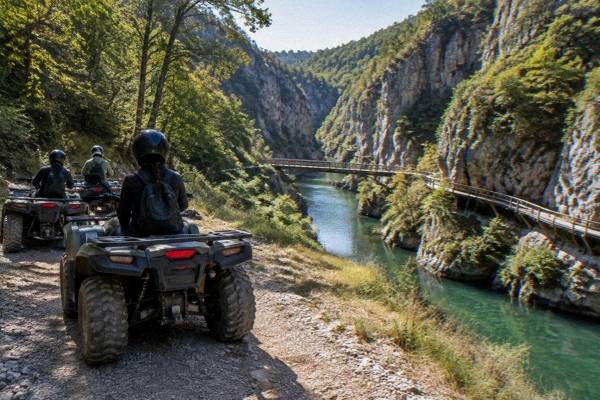 Quad bikes parked on a gravel trail beside a forest, helmeted riders seen from behind, Emen Canyon