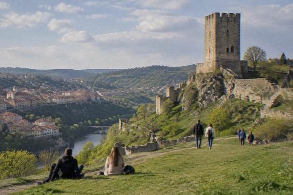 Day visitors on a grass slope below a tall square medieval tower on a rocky hill, early in the day, Baldwin's Tower