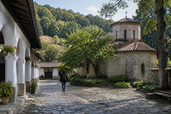 A lone visitor walking the cobbled yard of a walled monastery on a forested hillside, early in the day, Preobrazhenski Monastery