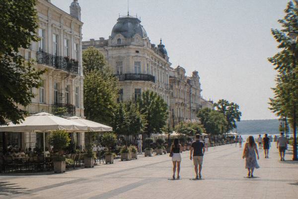 A small group strolling a broad pedestrian square lined with ornate late nineteenth-century buildings, Ruse