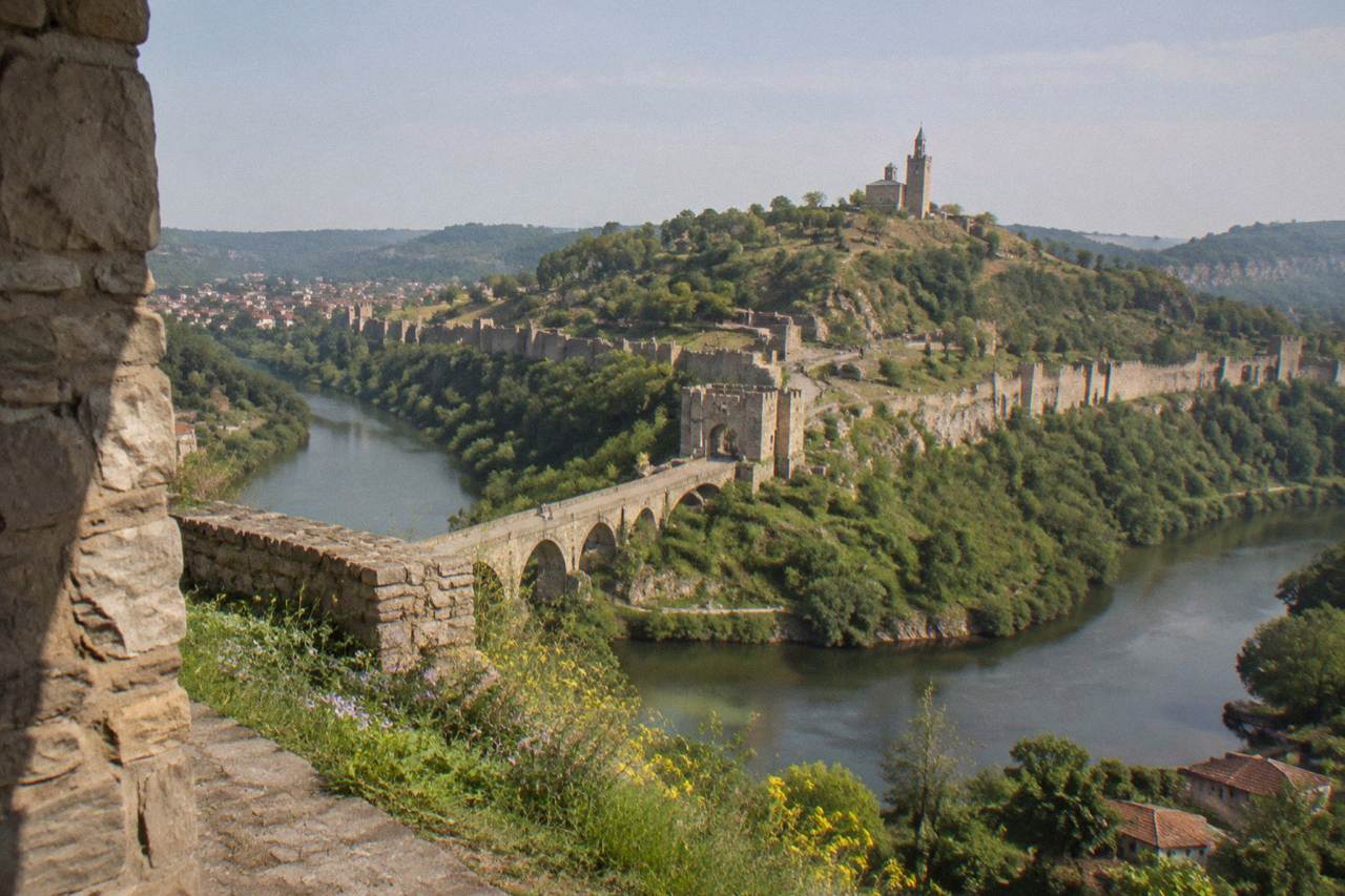 Stone fortress walls on a hill above a river bending around the old town of Veliko Tarnovo