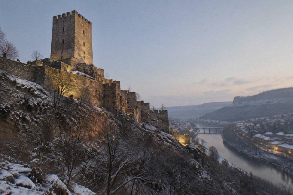 Evening lights playing across the walls of a fortress hill above a river town
