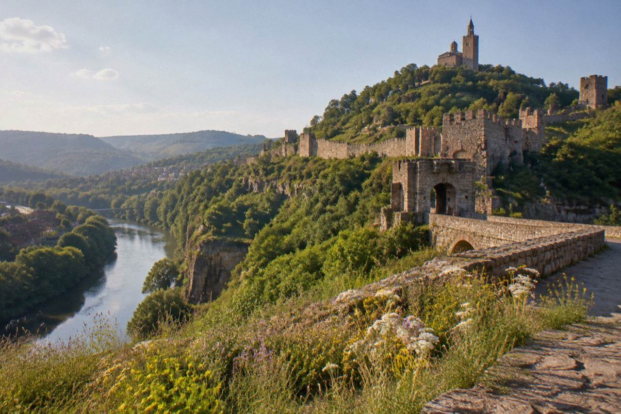 A hillside city with a fortress wall above a winding river at dusk