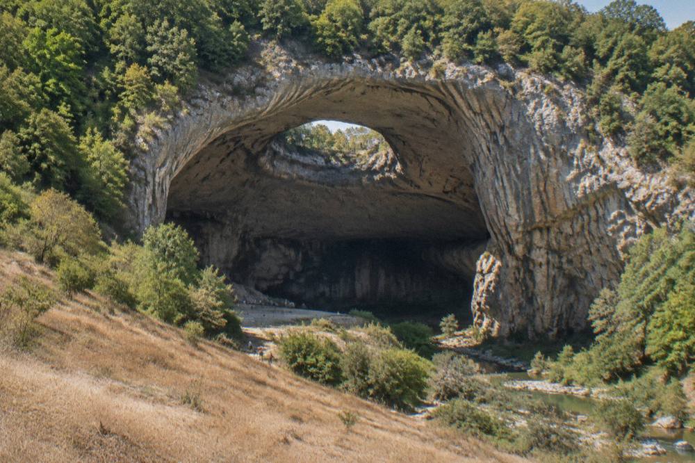 A cave entrance in a forested limestone hillside in northern Bulgaria