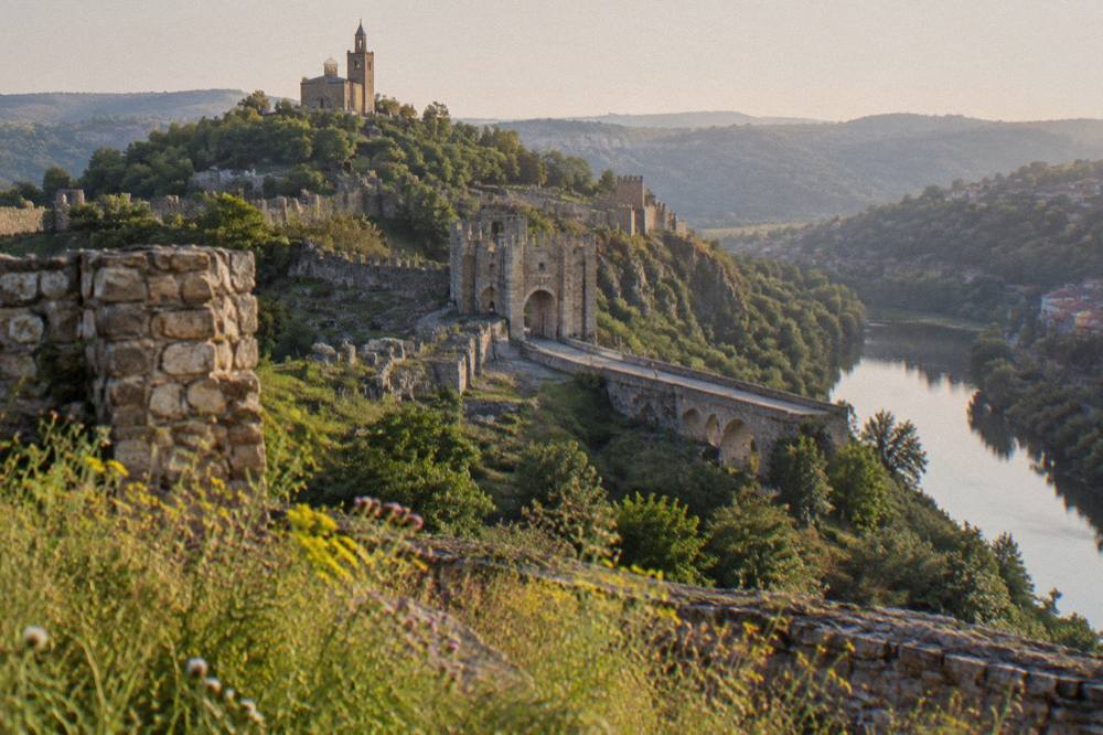 Stone fortress walls and a hilltop cathedral silhouette above a winding river at golden hour