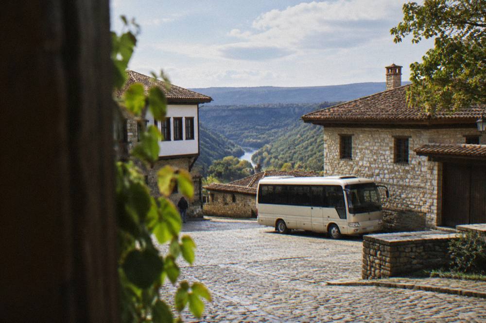 A small coach parked on a village square beside stone walls