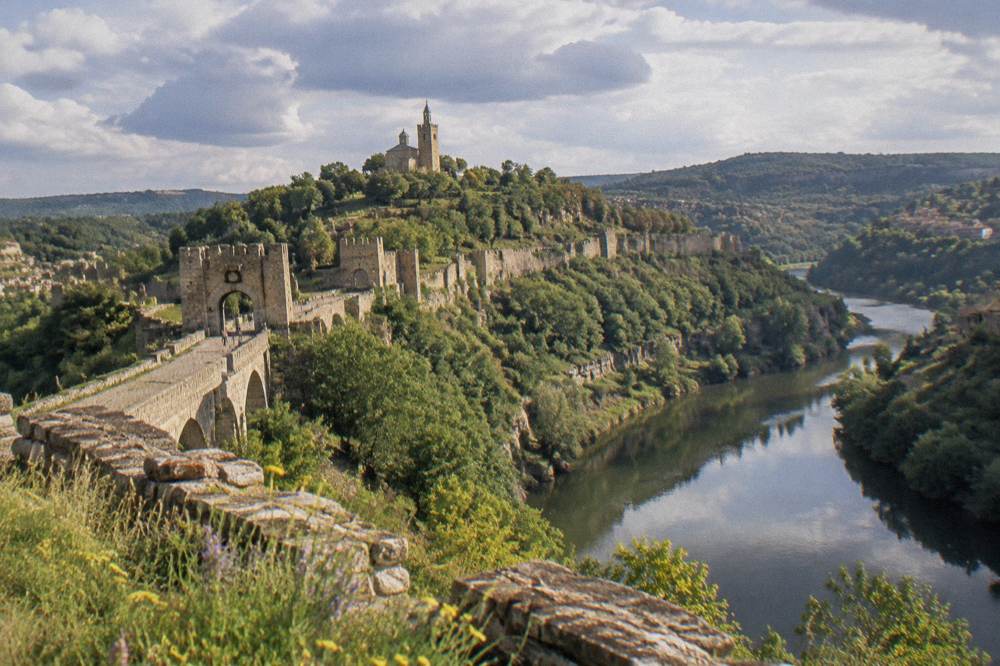 A riverside hill with fortress walls and a church tower seen across a deep river bend
