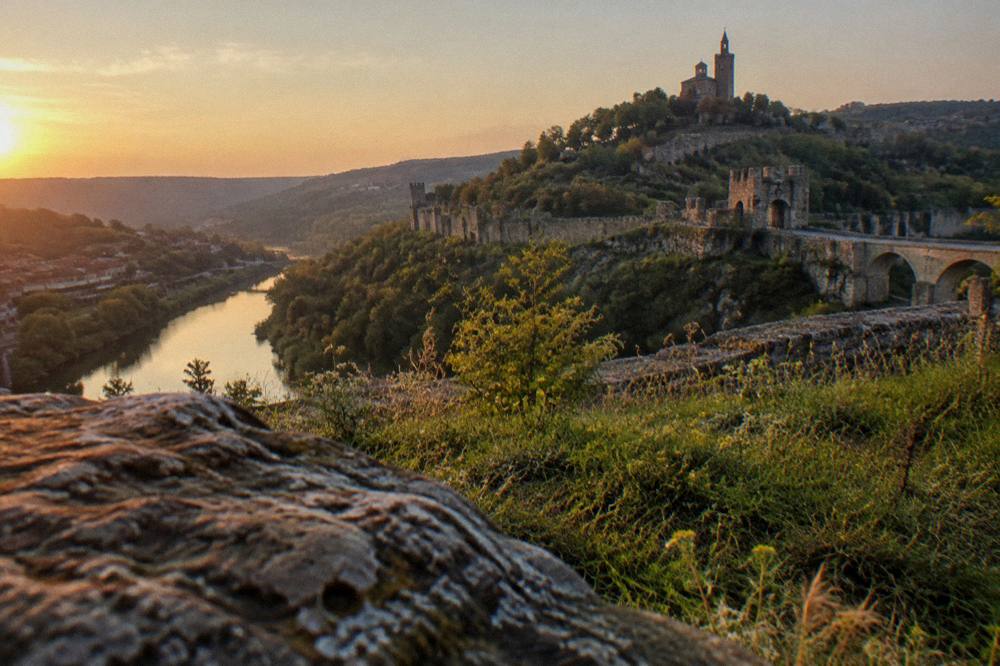 A fortress wall and hill silhouette at dusk above a river in a Bulgarian town