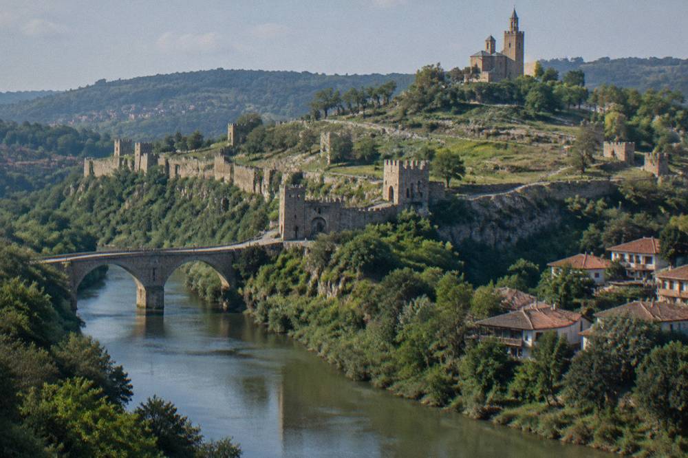 Fortress walls on a hilltop above a river with old houses on the slope below