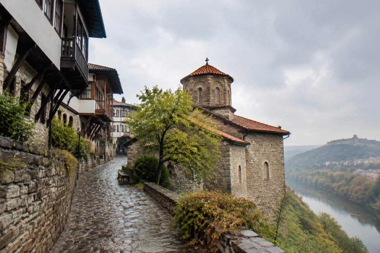 Stone church with a tiled roof beside a leafy path in Veliko Tarnovo