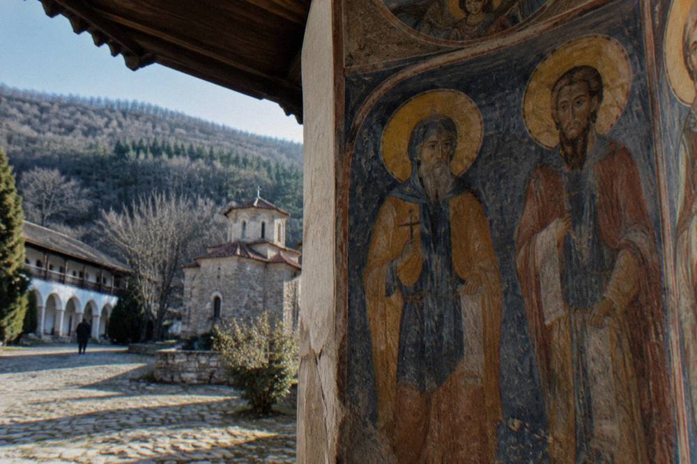 Close view of a fresco of saints painted on the interior wall of a monastery church, with warm ochre and blue pigments