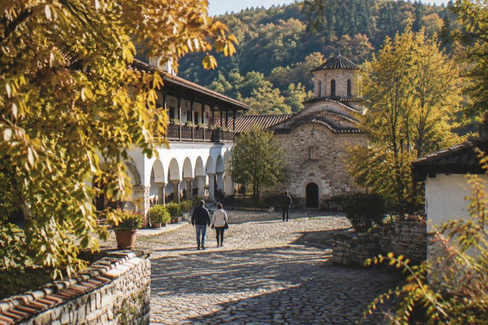 Autumn light on a monastery facade with golden leaves on the trees around a stone courtyard