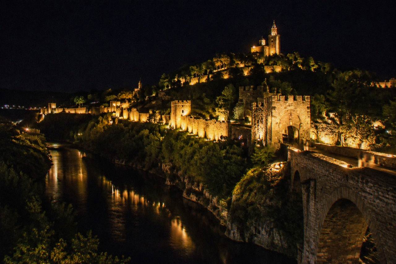 Fortress walls lit at night above a dark river valley