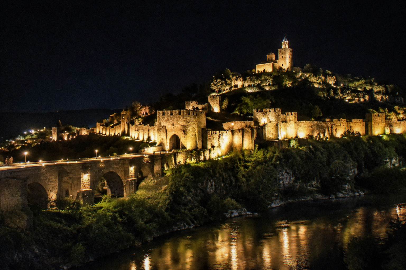 Floodlit fortress walls at night above the river valley