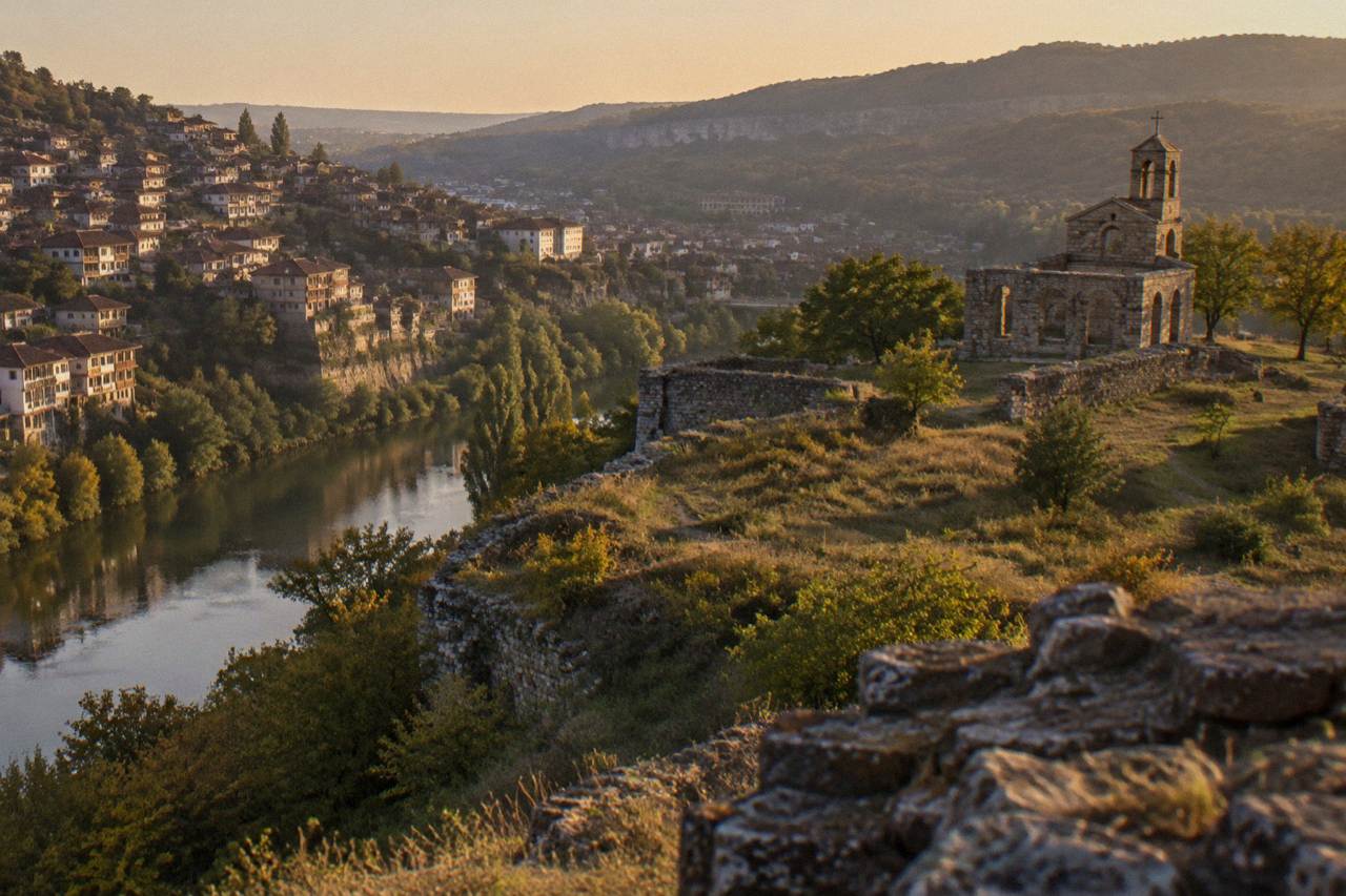 Houses stacked on a hillside above a curving river in a Bulgarian city at dusk