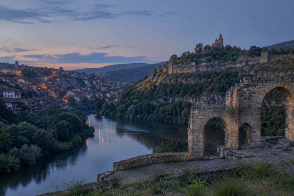 Stone monument with arches beside a river bend in the evening