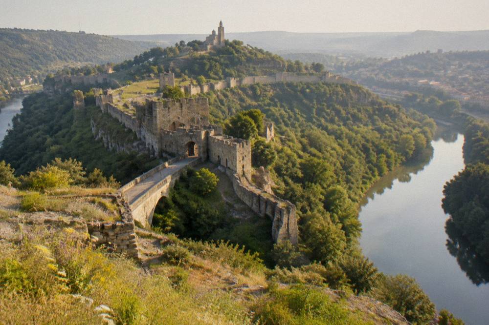 Medieval fortress walls on a hill above a winding river at golden hour