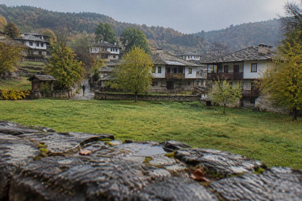 Village houses of Bozhentsi seen across a green meadow in rolling hills