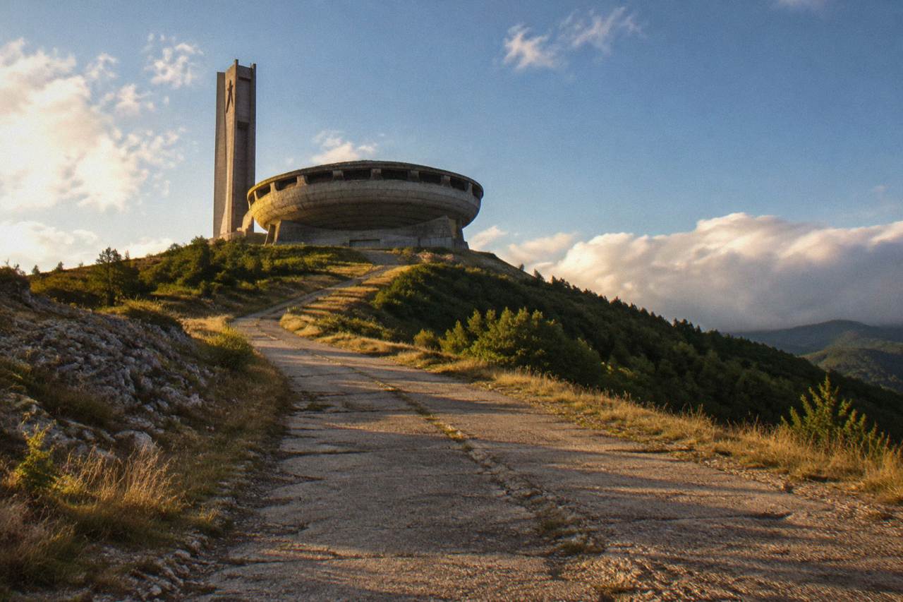 A saucer shaped concrete building standing on a green mountain peak under a wide sky
