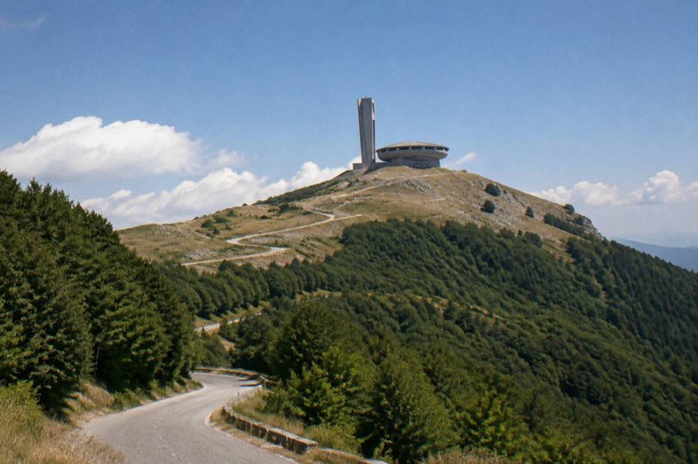 A winding mountain road climbing through forest toward a bare peak