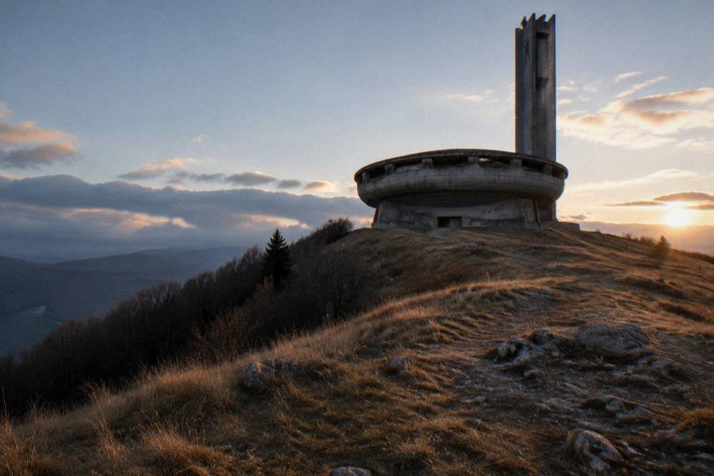 The concrete disc building seen from below on a grassy slope at dusk
