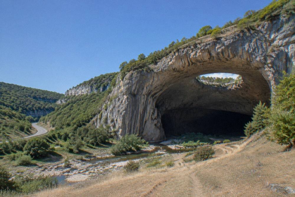 A rural road winding through green hills toward a limestone cliff
