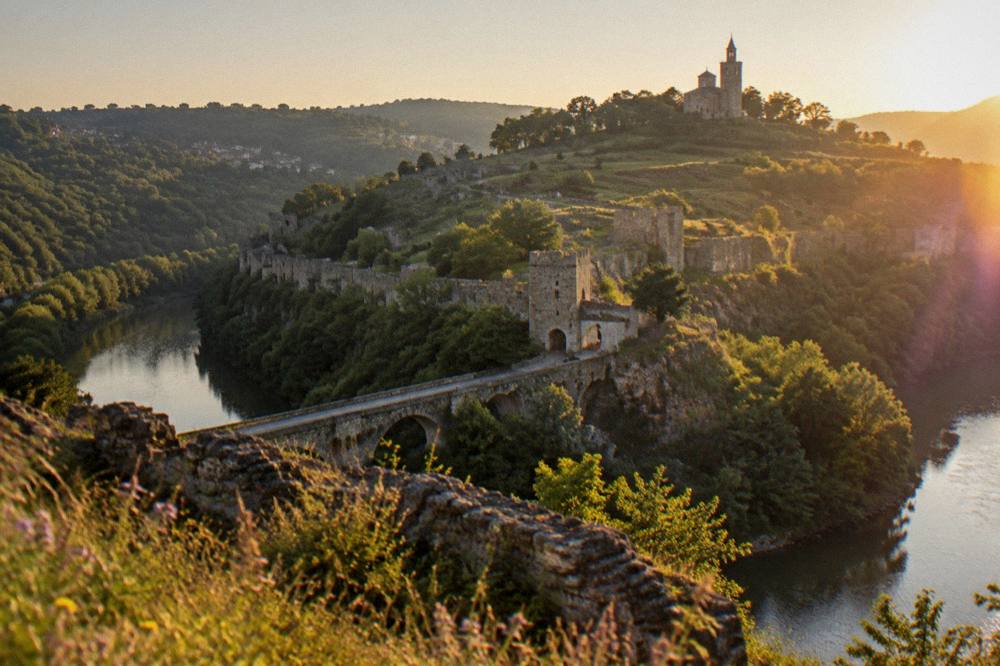 A stone fortress wall above a river bend at golden hour