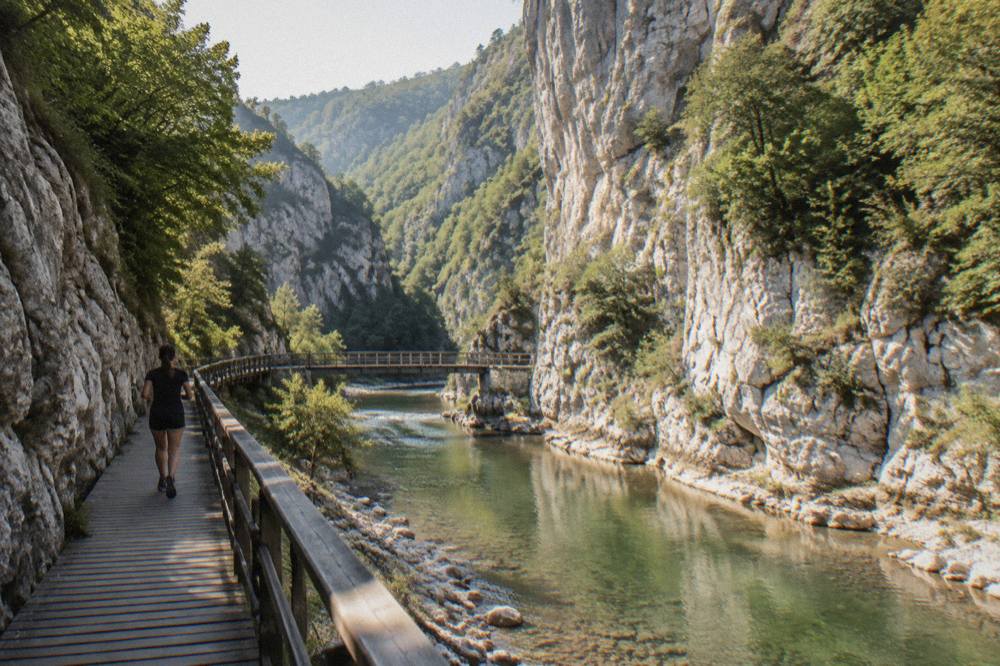White limestone cliff walls rising above a shallow green river with rounded stones along the bank
