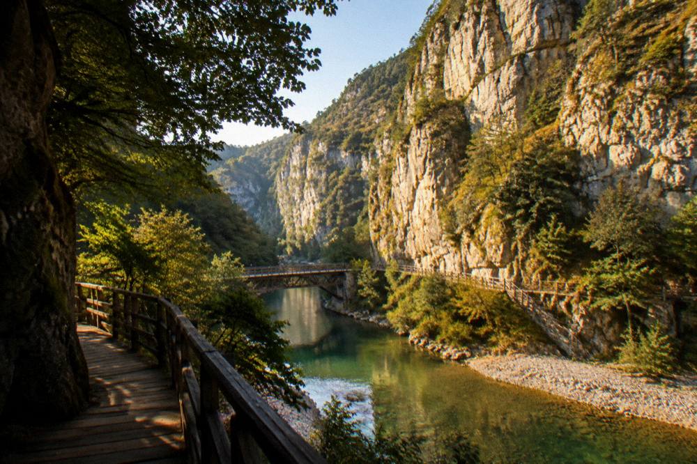 Sunlight falling on tall pale cliff faces above a narrow strip of green water and pebble beach