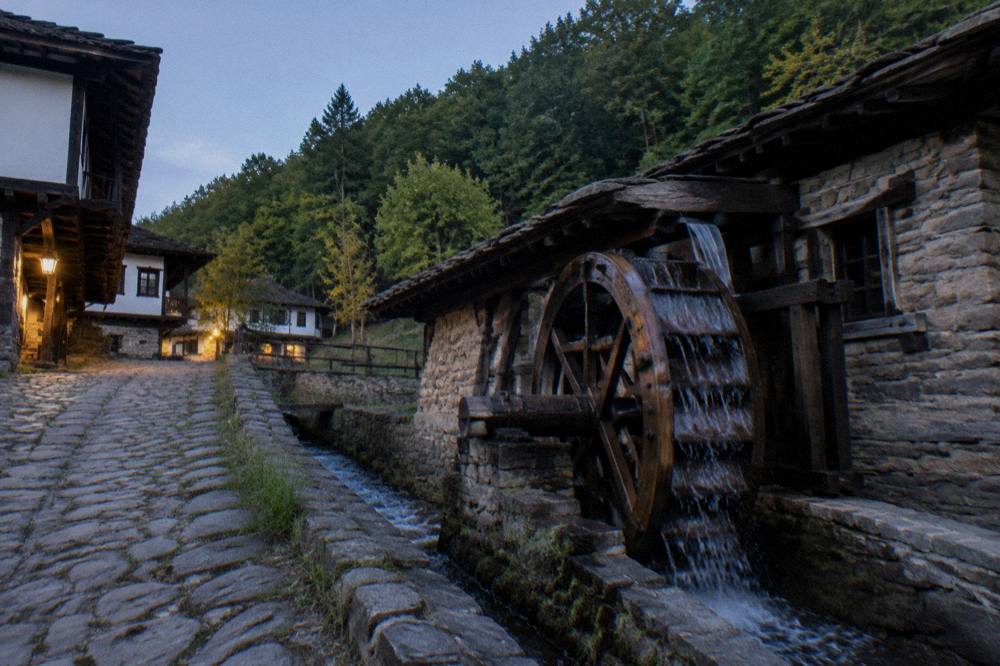 Wooden water wheel turning beside a stone channel in an open-air museum