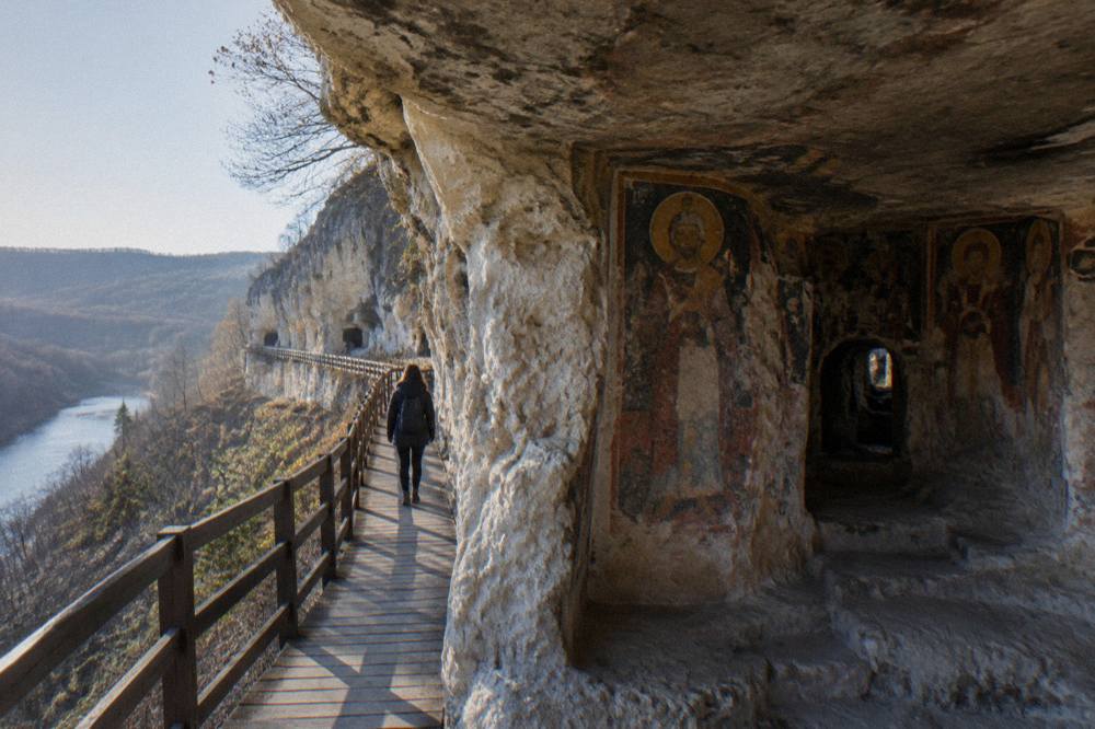 Interior of a cave church with faded medieval fresco figures on the rock walls