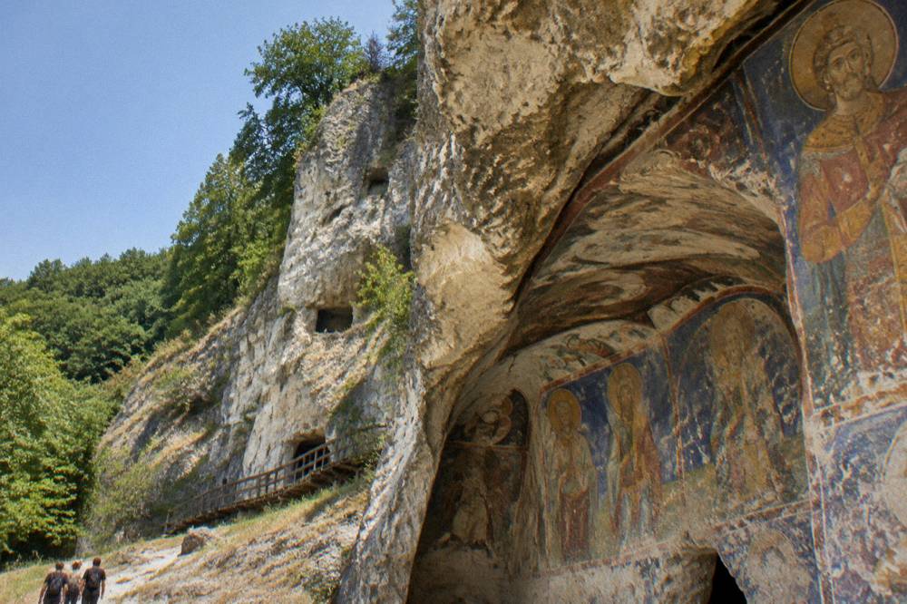 Brightly coloured medieval fresco portraits covering a curved rock-cut church wall