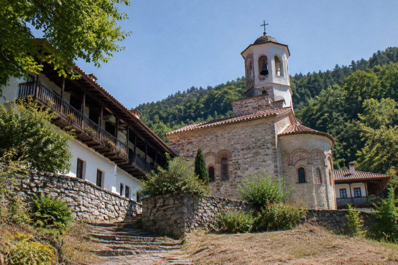 A monastery church with a tiled roof and a bell tower set among green hills