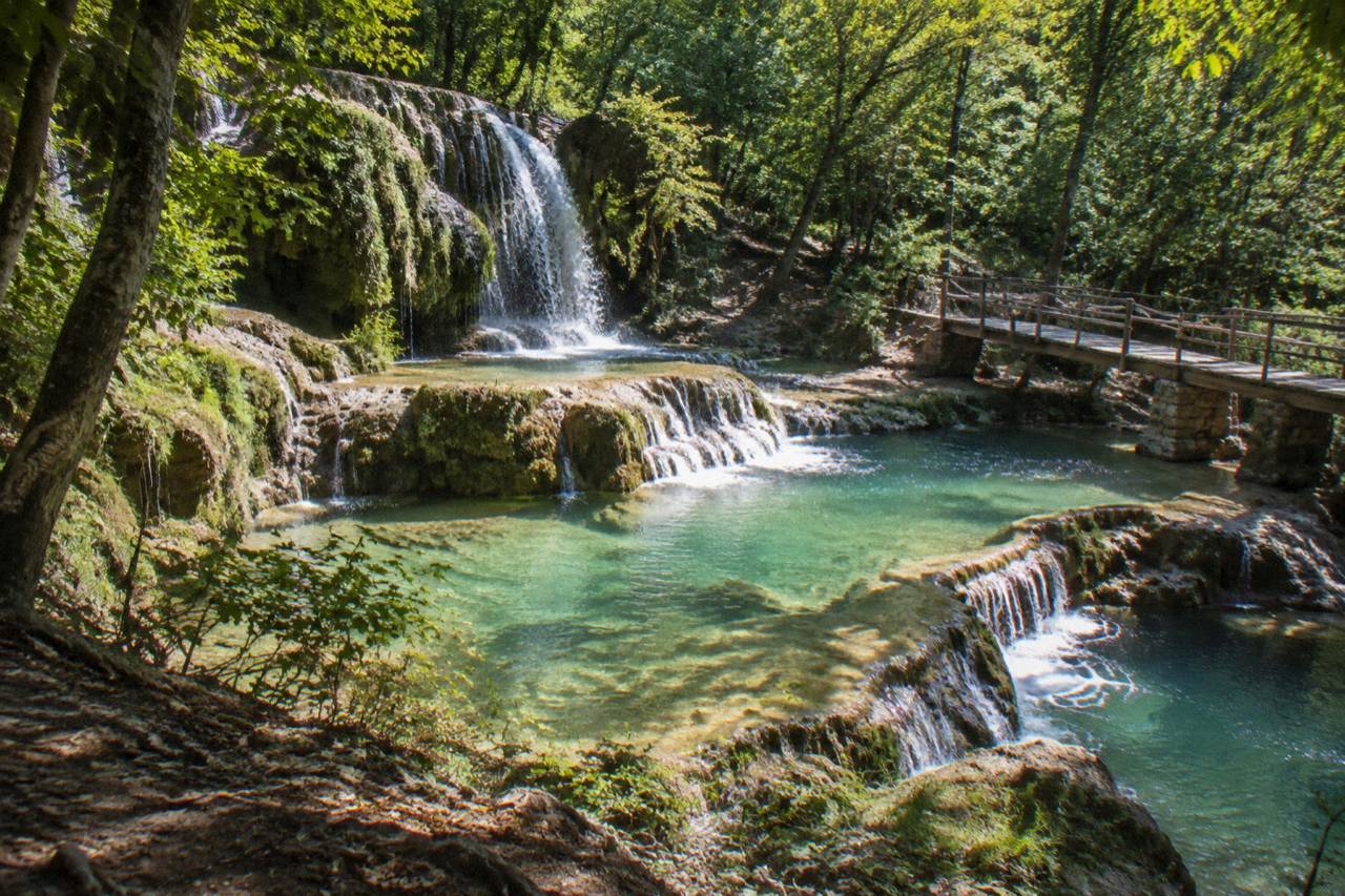 Terraced limestone pools of turquoise water stepping down a wooded hillside at Krushuna Falls