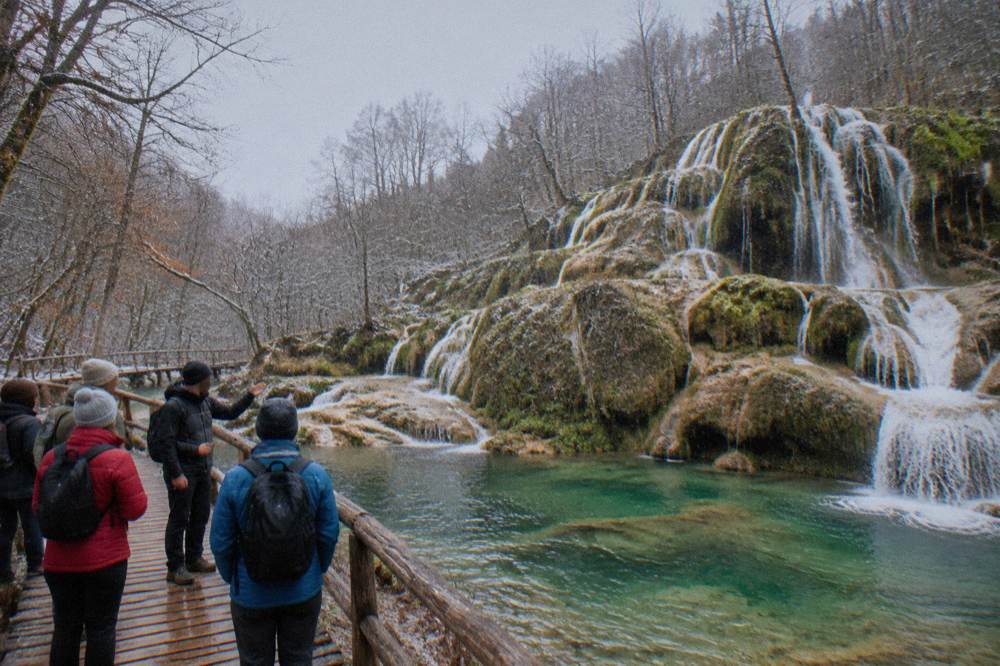 A guide speaking to a small group beside a waterfall while standing on a wooden walkway