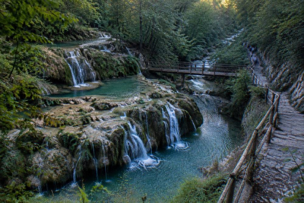 A stony path beside a stream with handrails winding through a narrow green gorge
