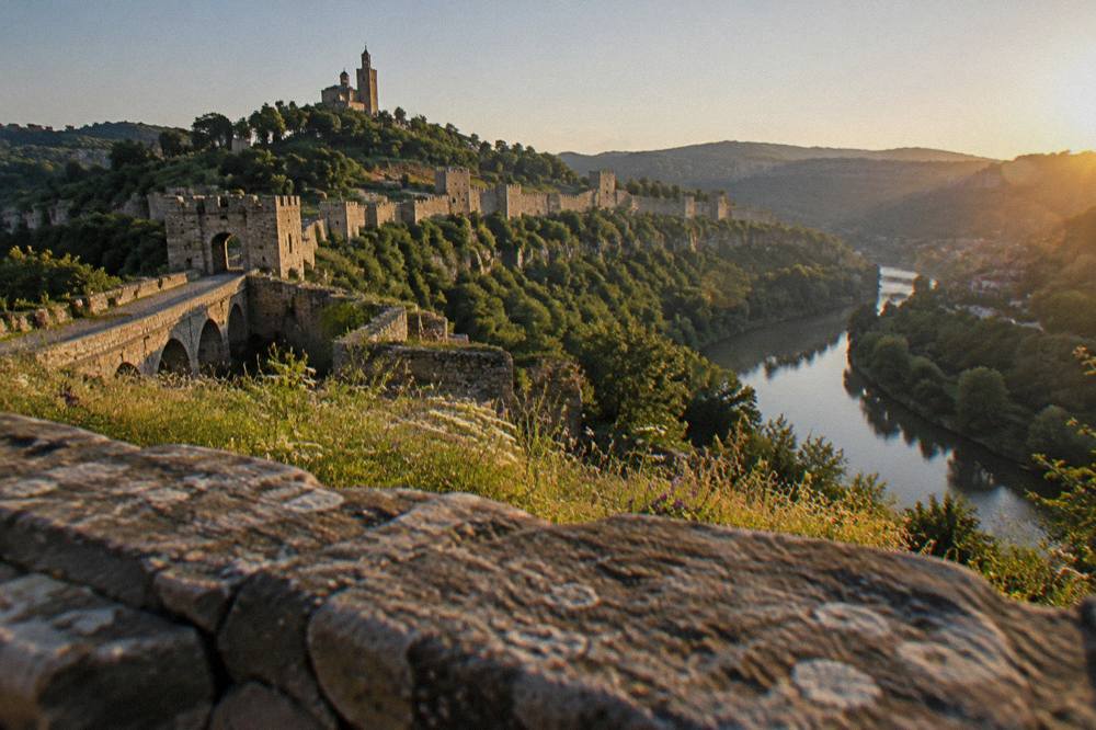 A hillside fortress wall above a river bend seen from a viewpoint in the evening