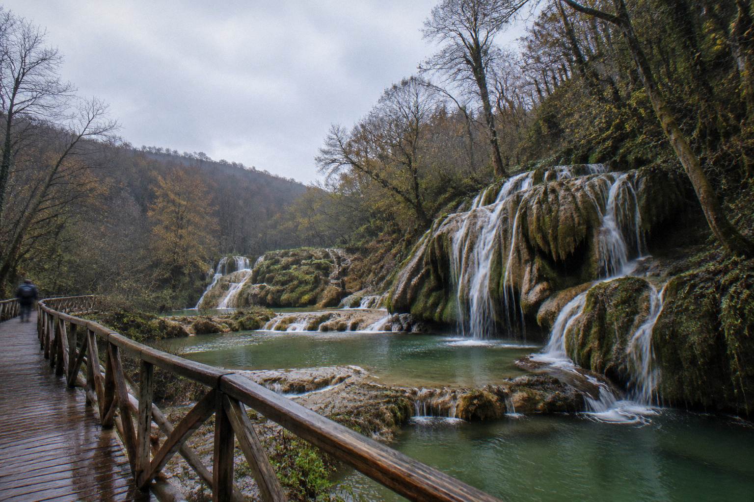 Travertine waterfall cascading into green pools in a wooded gorge