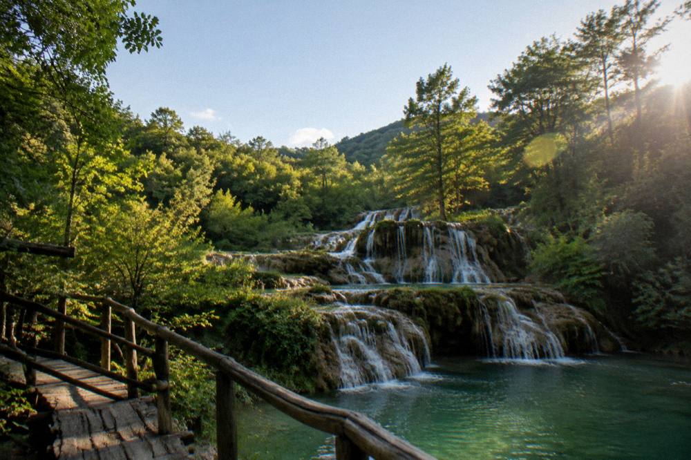 Stepped limestone waterfalls with turquoise pools in a wooded karst gorge