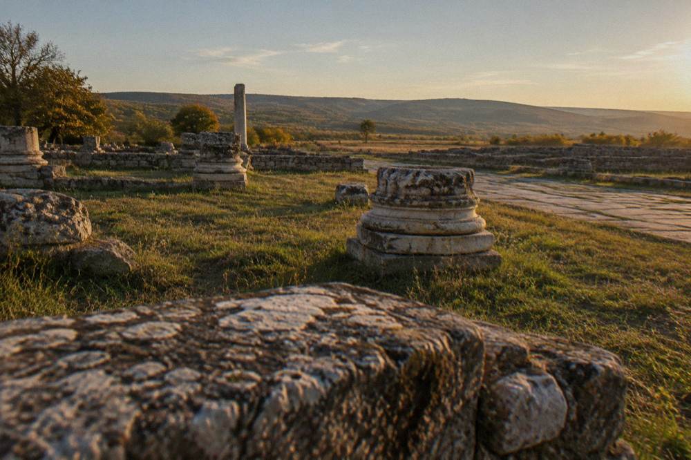 Weathered stone blocks and column bases resting on a grassy archaeological site