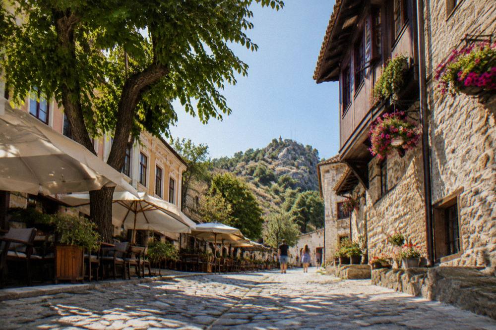 A cobbled old street with stone houses and hanging flowers in morning light