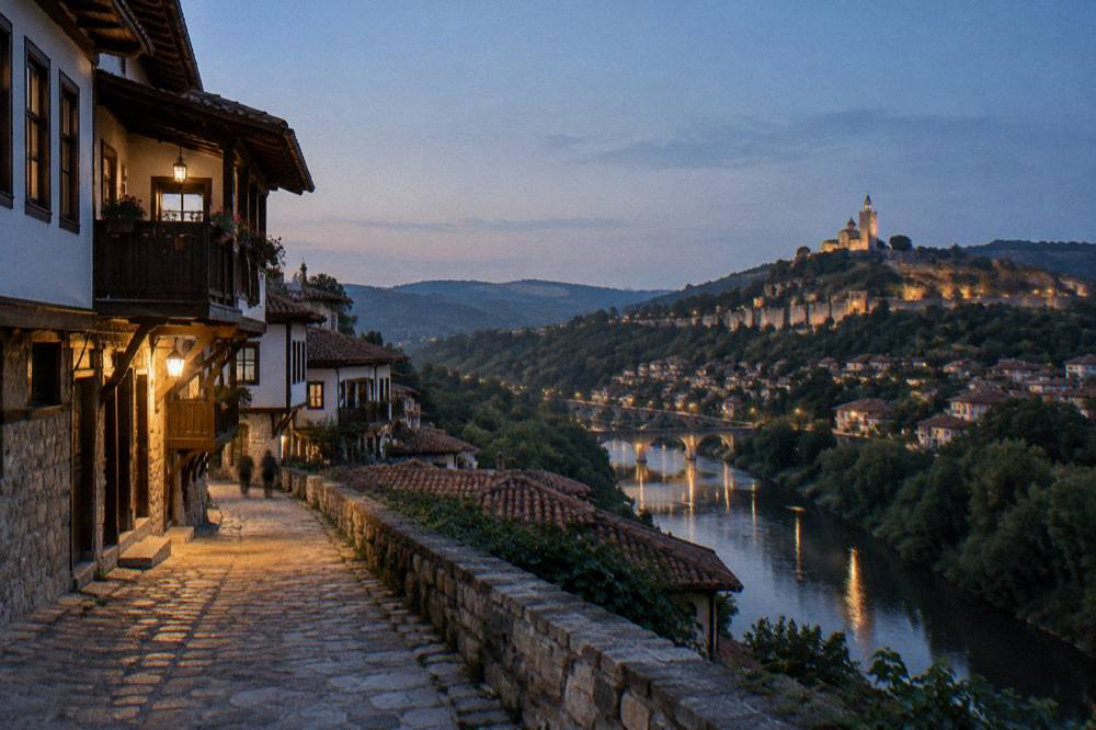 An evening panorama of a hilltop old town with lit streets and a river below