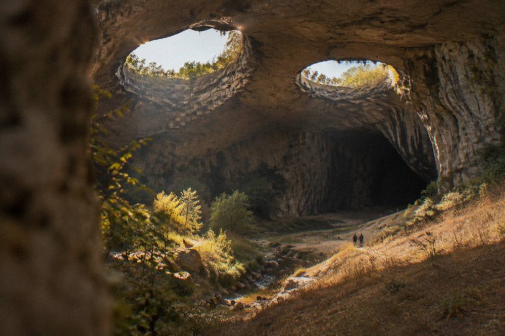 Two round openings in a cave ceiling glowing with daylight above dark rock walls