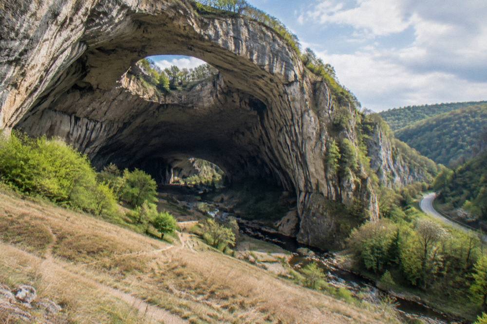 A rural road winding through green hills in north Bulgaria toward limestone cliffs
