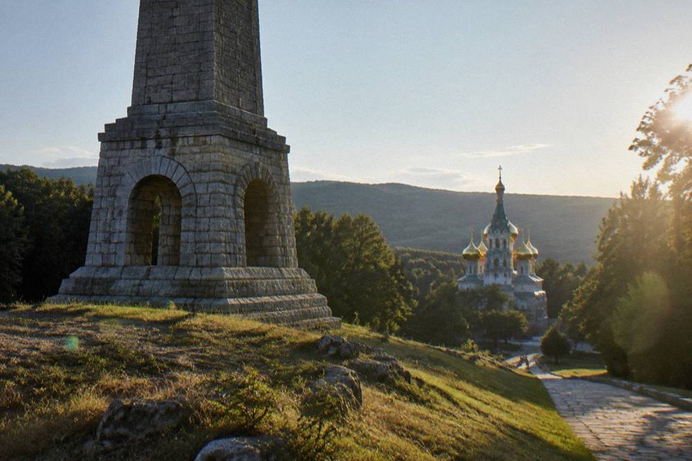 Close view of a tall stone monument with an arched base on a grassy summit