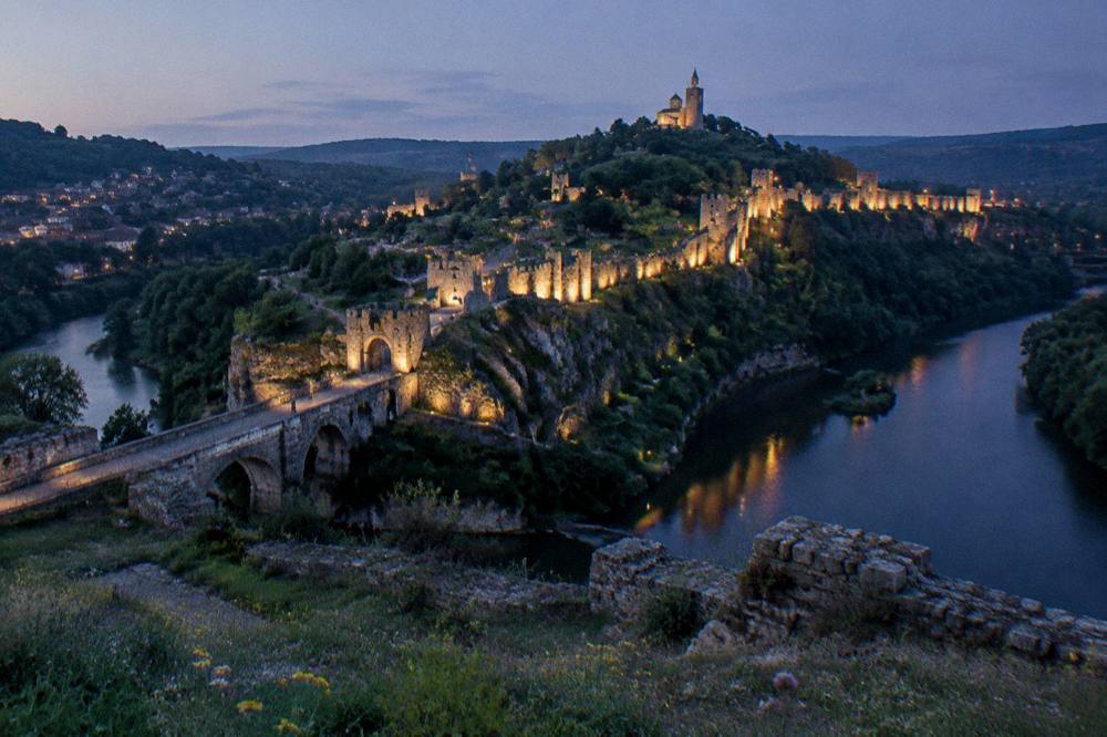 Illuminated fortress walls above a dark river bend at night