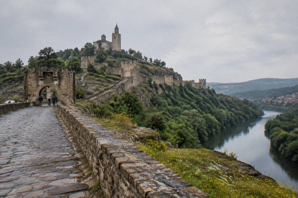 Stone fortress walls and a bell tower on a hilltop above a river