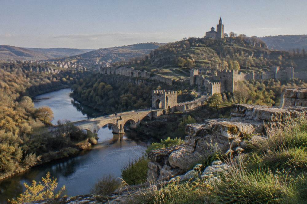 Stone fortification walls of Tsarevets rising above the river in late afternoon light
